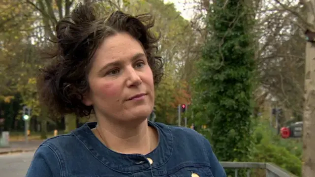 Claire Hanna MP wearing a denim jacket, standing in a park