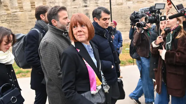 Gisèle Pelicot looks over her shoulder and smiles as she walks along, surrounded by camera crew