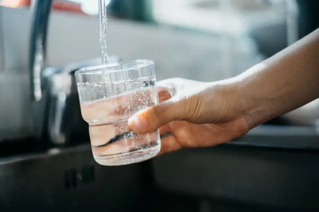 Close up of a woman's hand filling a glass of filtered water right from the tap in the kitchen sink at home