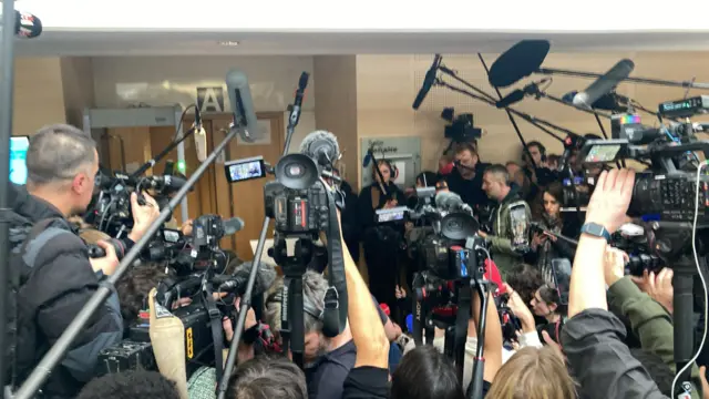 Camera crews huddle around a set of double doors in court