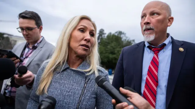 Rep Marjorie Taylor Greene answers questions from reporters hold microphones as she stands outside with Rep. Chip Roy.