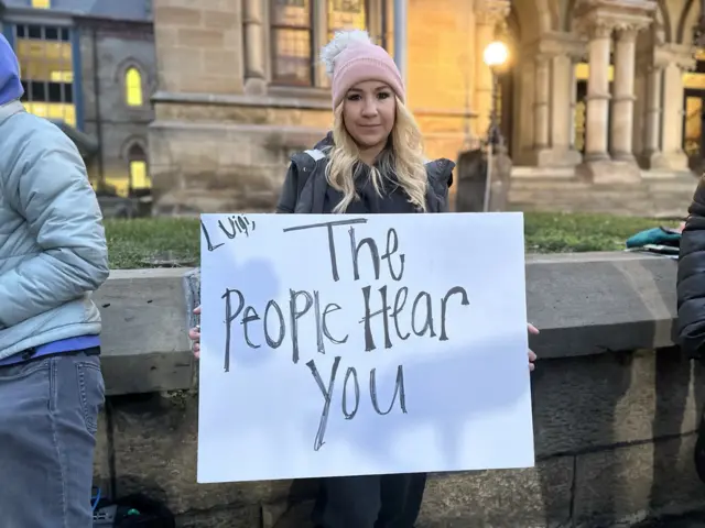 April holds a sign that reads 'Luigi the people hear you' outside a courthouse in Pennsylvania