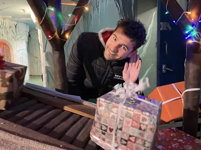 Charlie Taylor standing behind a present conveyor belt with his hand to his ear