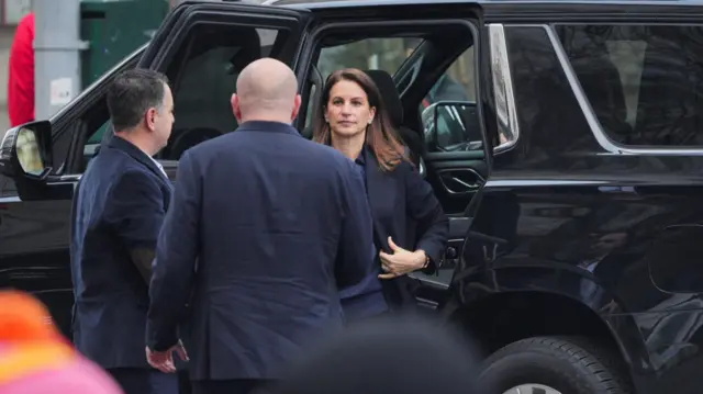 A woman leaves a black SUV while two men face her