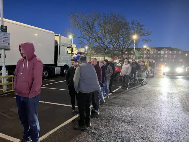 A line of people queueing in the dark in a car park