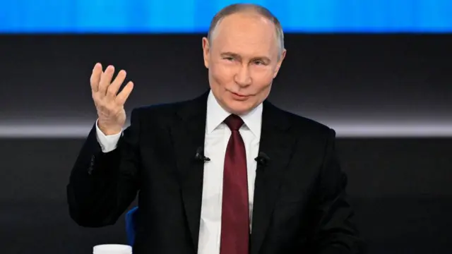 President Putin raises his hand while speaking at an event.