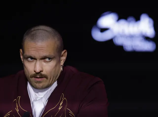 Oleksandr Usyk in a maroon suit speaks to the media