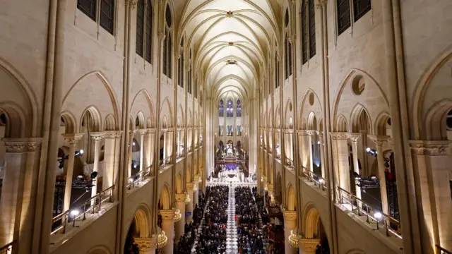 General view of the nave of the Notre-Dame de Paris Cathedral, with restored limestone walls, and seats full of people looking ahead for the reopening ceremony