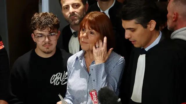 Pelicot adjusts her hair as she stands in front of microphones, surrounded by family, journalists and lawyers