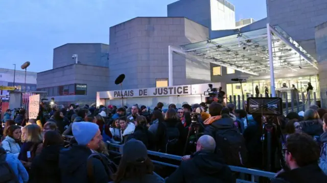 Large queue of people crowds the outsides of the Palais de Justice