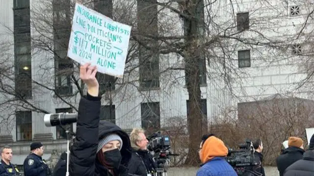 Protestor holding a sign saying 'insurance lobbyists line politicians' pockets'