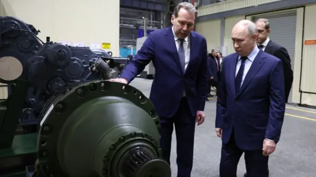 Russia's president looks at part of a tank during a visit to a factory