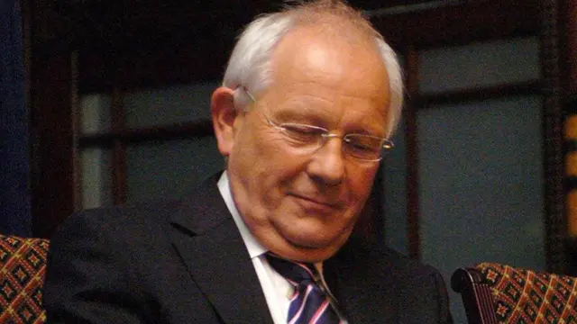 Sir Duncan Nichol wearing black suit sat in patterned chair