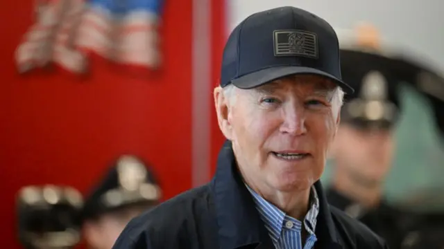 Joe Biden speaks to reporters after greeting police and fire personnel. He's wearing a black cap, black jacket and striped shirt