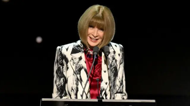 Anna Wintour in a black and white blazer and red shirt - without her trademark sunglasses