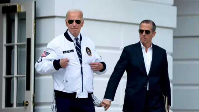 Joe Biden in White Jacket and blue trousers leaves White House to board helicopter with son Hunter in dark suit and white shirt walking next to him as he holds hand with his aunt Valerie Biden (hidden behind president)