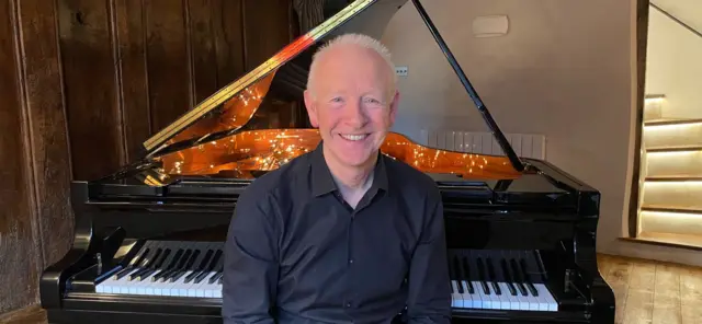 Grey haird man sat in front of piano