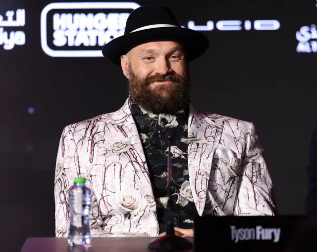 A bearded Tyson Fury smiles at a news conference