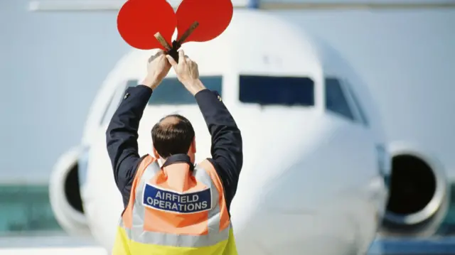 An airtraffick controller signals a plane to stop