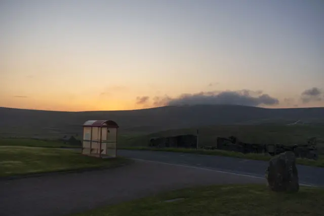 A picture of a sunset over rolling hills. A bus stop is in the foreground