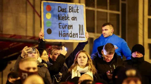 Group of protestors with a sign in German saying 'the blood sticks to your hands!'