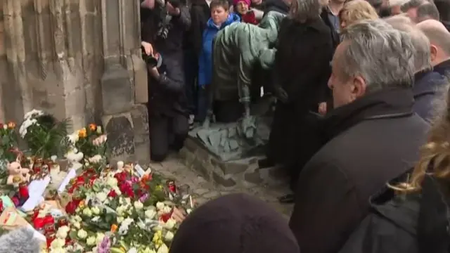 Several bunches of flowers on the ground with a group of people stood in front of them