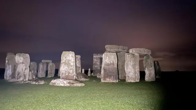 Stonehenge in the darkness, the sky has a red tinge and it's lit up by floodlights