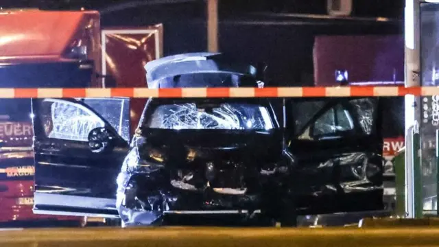 The front of a smashed up black BMW car, with all of its doors wide open, behind red and white tape