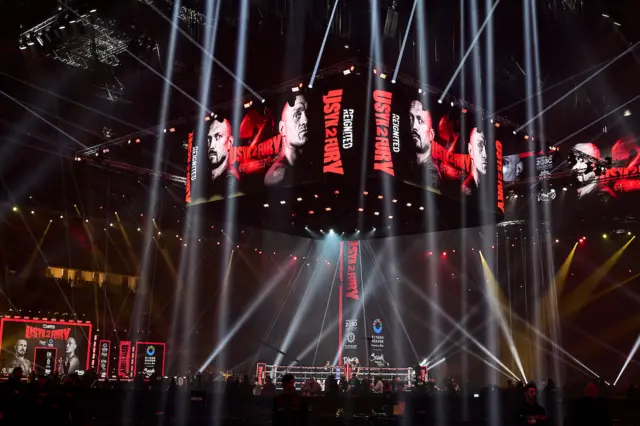 A screen showing Oleksandr Usyk and Tyson Fury above a boxing ring