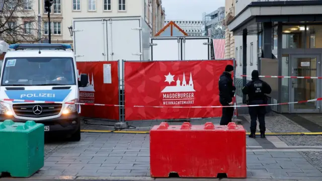 A green and red boulder sit in front of an advertisement for Magdeburg, with two police stood with their backs to the camera