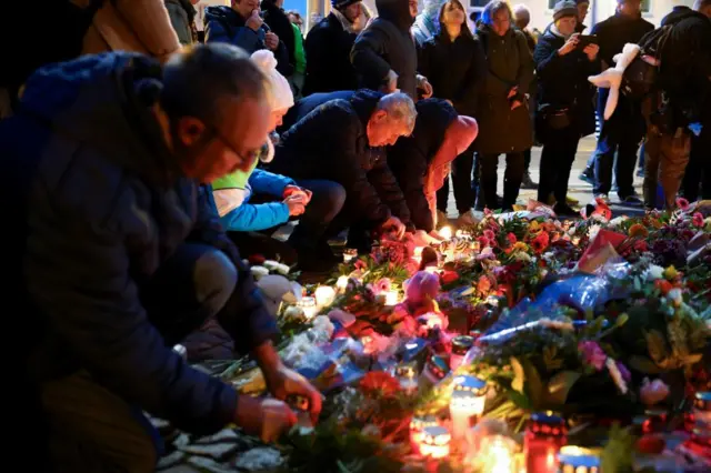 People leave candles and floral tributes to the victims near the site where a car rammed into a crowd at a Magdeburg Christmas market in Magdeburg