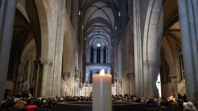 Wide view of Magdeburg cathedral, looking at the backs of the seated congregation with a blurred lit candle in the middle foreground