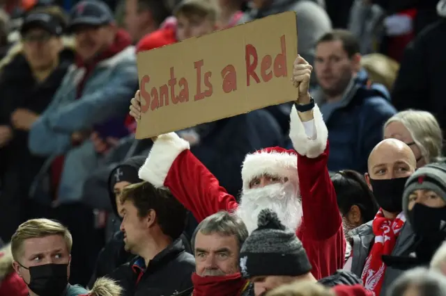 A Liverpool fan dressed as Santa holding up a sign saying Santa is a red