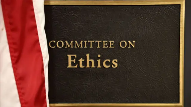 Leather and gold plaque marked Committee on Ethics with a portion of US flag visible to the left of the frame