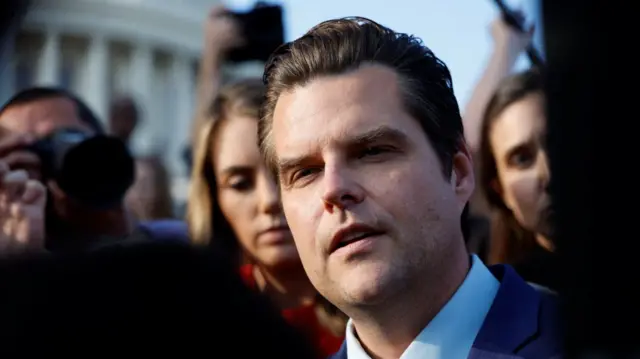 Matt Gaetz close up. He's standing speaking to the press outside of Congress, with the outside of the rotunda visible in the background. Members of the press holding hand-held mics and cameras are visible around him