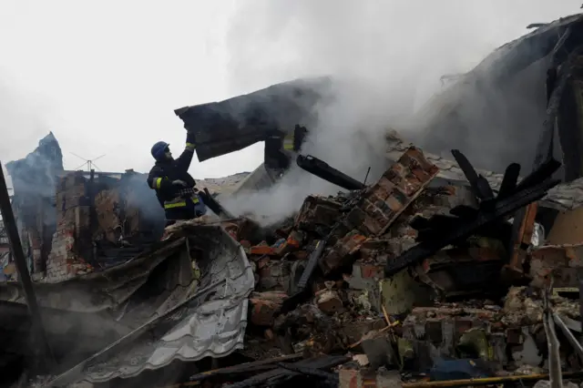 Firefighters lift rubble in the middle of flattened buildings.