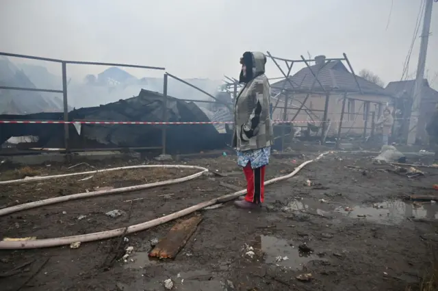 woman in grey coat looks at the damage done to her neighbour's house in Kharkiv