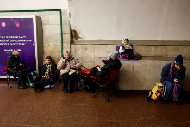 Women sitting on chairs and a girl on a wall in a metro station in Kyiv