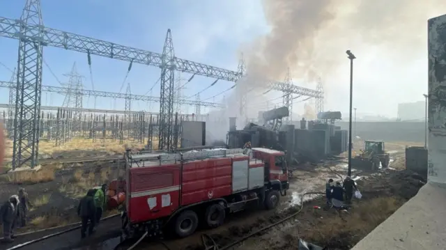 A damaged power station with smoke billowing from it and a big red fire engine