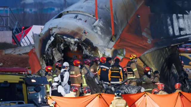 Rescue and inspection members in front of the wreckage of Jeju Air Co. Flight 2216 at Muan International Airport