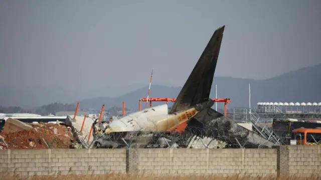 The tail of the plane can be seen behind a wall with barbed wire