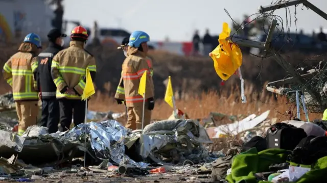 Emergency service personnel stand in high-vis clothing. Debris is on the floor and a life jacket hangs on fencing