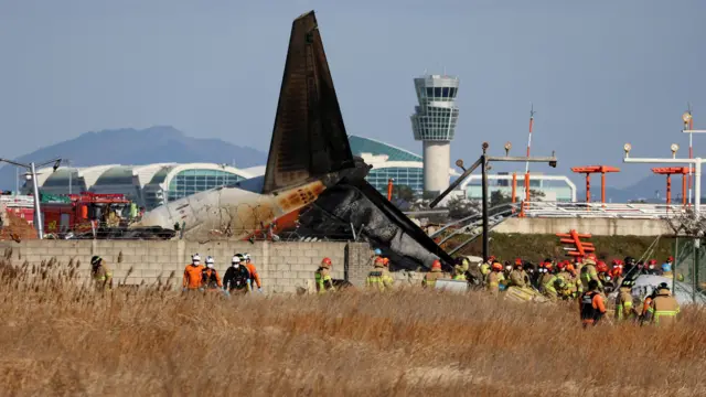 Firefighters are seen around an aircraft which drove off runway at Muan International Airport