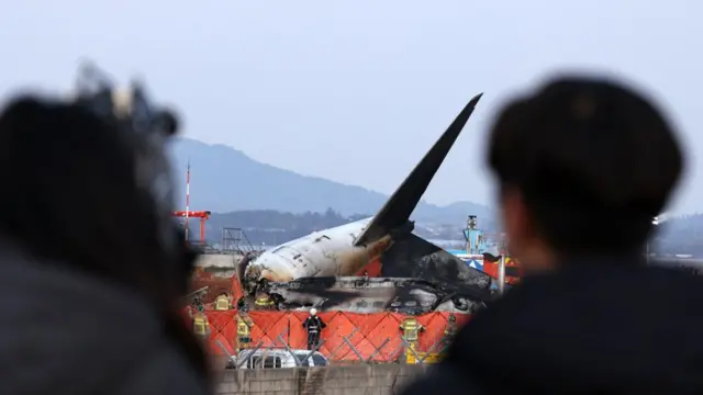 People look on as firefighters search at the wreckage of the Jeju Air aircraft at Muan International Airport in Muan