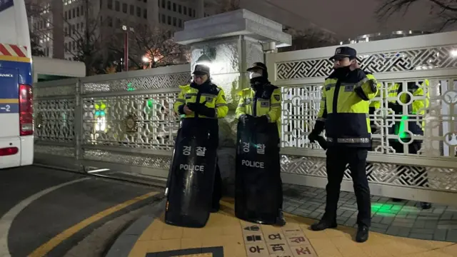 Police officers holding shields stand outside railings near the National Assembly