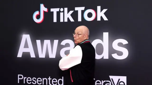 A man poses for a photograph with 'TikTok Awards' written on a display in the background.