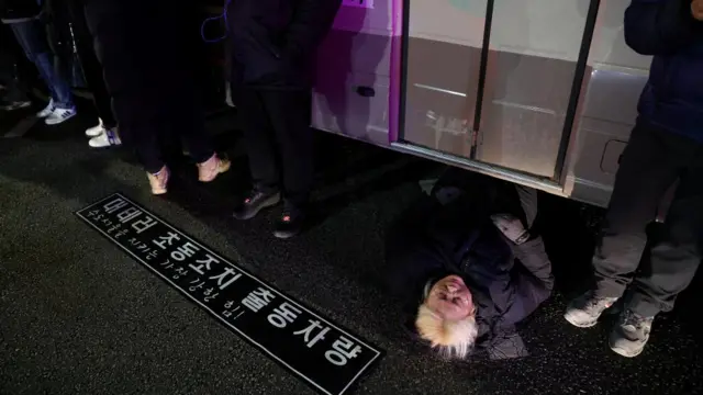 A woman lies on a road to block a vehicle transporting an army unit, after South Korean President Yoon Suk Yeol declared martial law