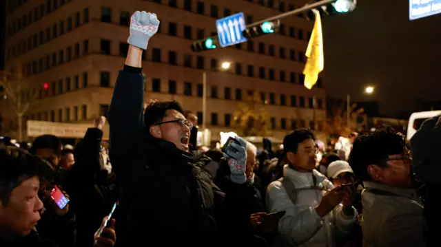 A person gestures while standing among the crowd outside the National Assembly