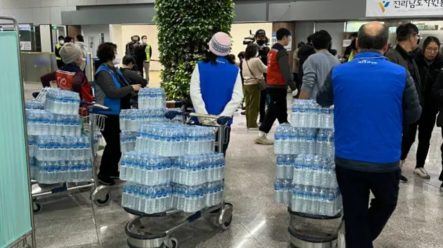 People gather with cases of bottles of water at the airport