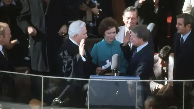 Carter, right, holds his hand up as he mirrors Chief Justice Warren Burger. Rosalynn, in a team coat, stands behind them